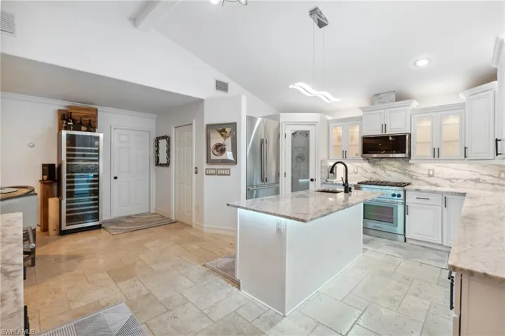 Kitchen with high quality appliances, a center island with sink, white cabinets, and decorative light fixtures