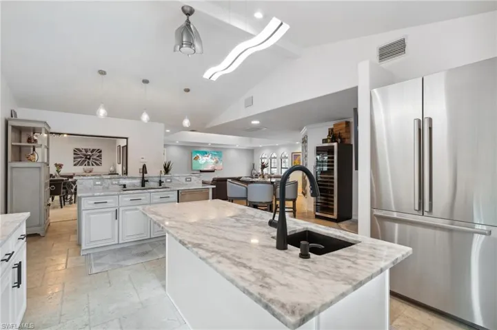 Kitchen with light stone countertops, stainless steel fridge, a large island with sink, pendant lighting, and wine cooler