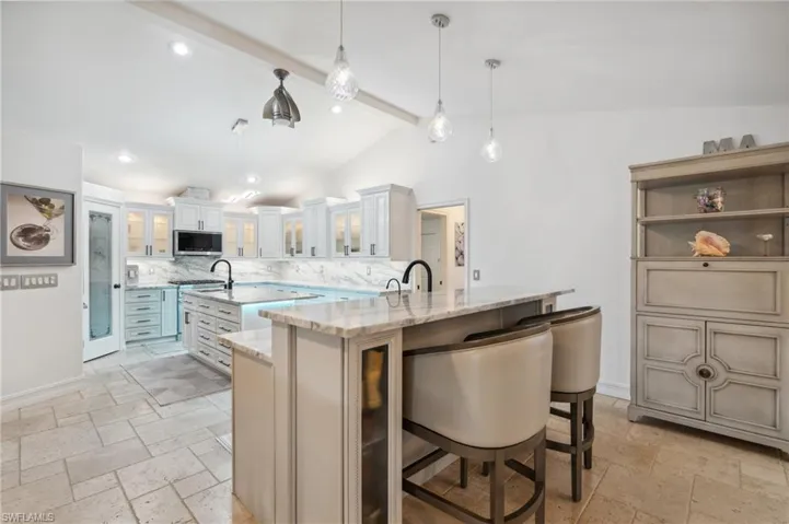 Kitchen featuring light stone countertops, lofted ceiling with beams, a spacious island, pendant lighting, and a breakfast bar