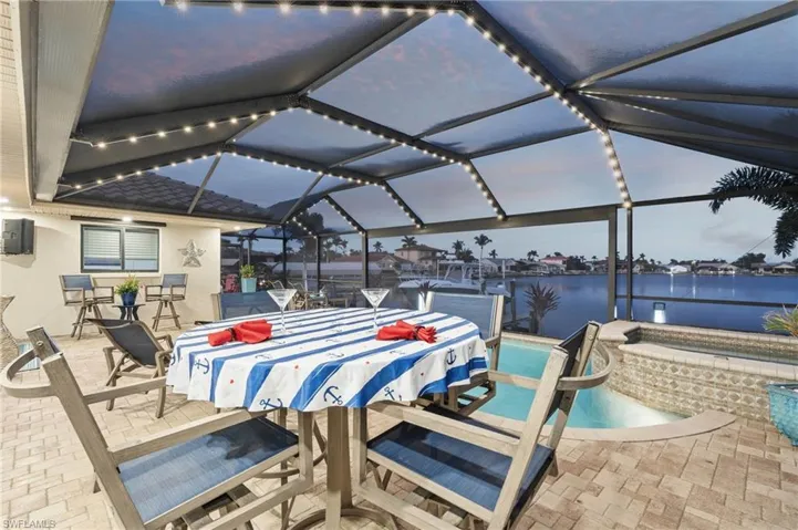 Patio terrace at dusk with a water view, an outdoor bar, and a lanai