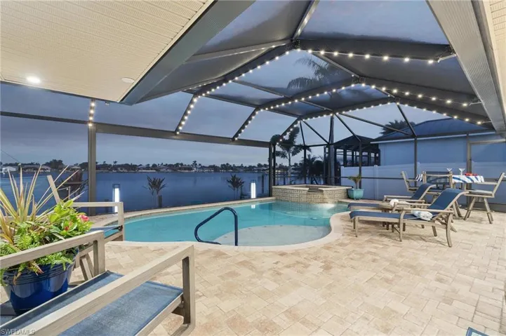 Pool at dusk with a lanai, a water view, a patio, and an in ground hot tub