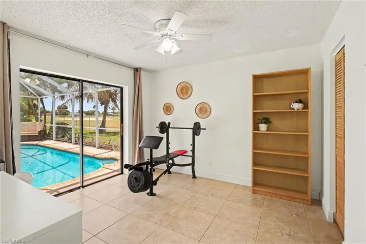Room with sliding glass doors opening to a screened pool area, featuring a built-in wooden shelving unit, ceiling fan, and tiled flooring