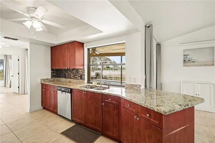 Kitchen featuring wood cabinetry, light-toned granite countertops, a mosaic tile backsplash, and a double-basin stainless steel sink