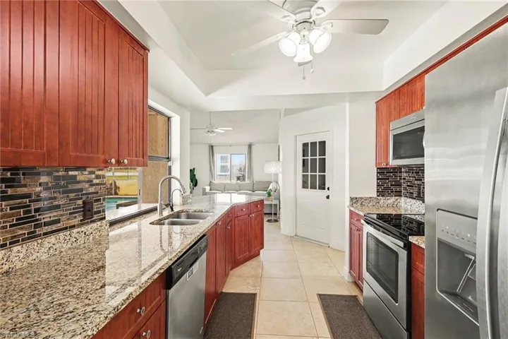 Kitchen featuring wood cabinetry, light granite countertops, stainless steel appliances, a mosaic tile backsplash, and a double basin sink