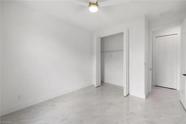 Unfurnished bedroom with light marble finish floors, ceiling fan, and a closet
