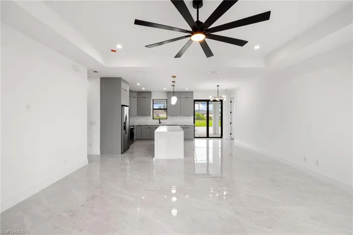 Unfurnished living room with a raised ceiling, recessed lighting, light marble finish flooring, ceiling fan, and a chandelier