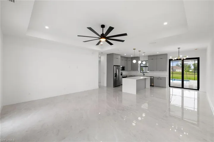 Unfurnished living room with a raised ceiling, a ceiling fan, recessed lighting, light marble finish flooring, and a chandelier