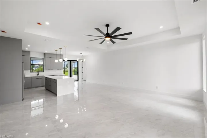 Unfurnished living room with a tray ceiling, ceiling fan, recessed lighting, and a chandelier