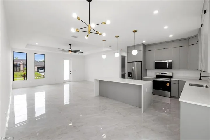 Kitchen with appliances with stainless steel finishes, gray cabinetry, a chandelier, modern cabinets, and a kitchen island