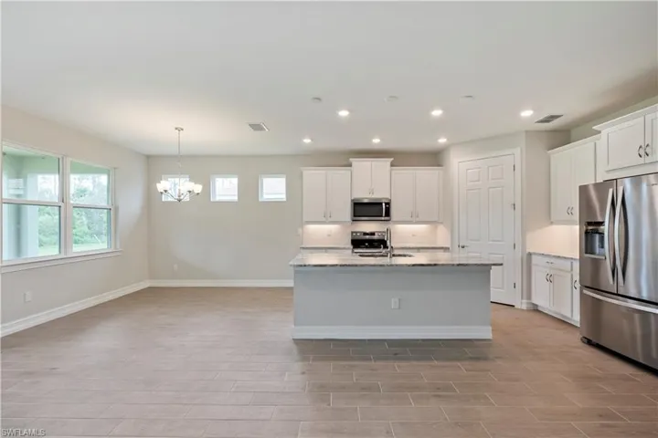 Kitchen featuring white cabinetry, an inviting chandelier, light stone counters, a center island with sink, and appliances with stainless steel finishes