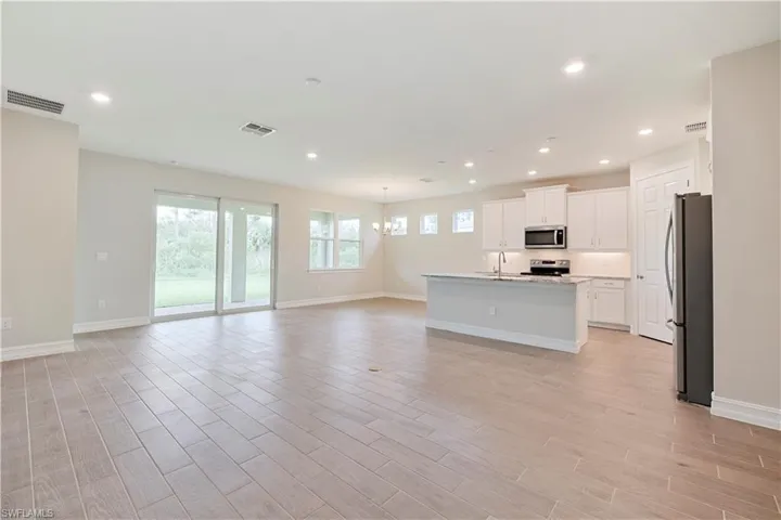 Kitchen with appliances with stainless steel finishes, white cabinetry, a healthy amount of sunlight, and a kitchen island with sink