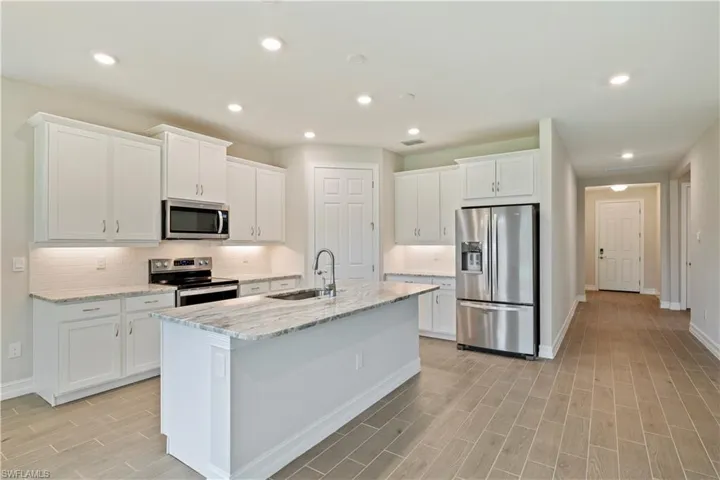 Kitchen with white cabinetry, stainless steel appliances, sink, decorative backsplash, and a center island with sink