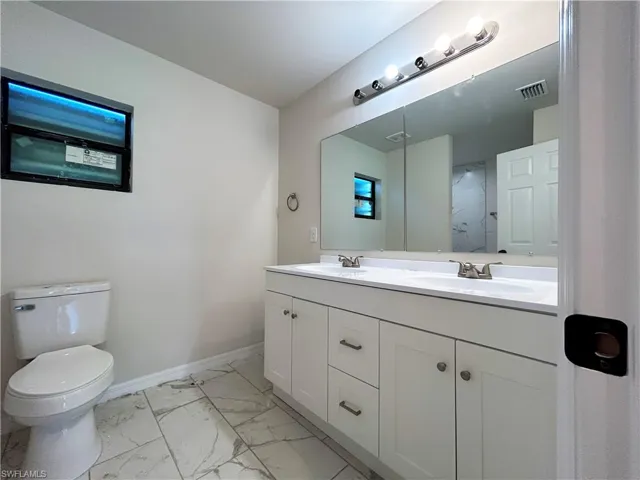 Bathroom with tile flooring, double sink, toilet, and vanity with extensive cabinet space