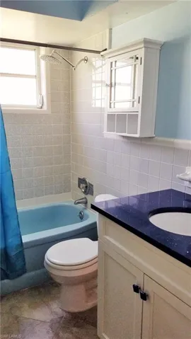 Full bath with shower / bath combo with shower curtain, vanity, tile walls, and backsplash