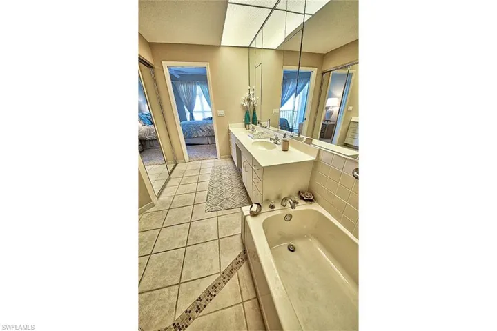 Full bathroom with ensuite bath, light tile patterned floors, a bath, double vanity, and a textured ceiling