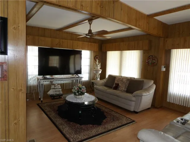Living area with ceiling fan, wood finished floors, wooden walls, and beam ceiling
