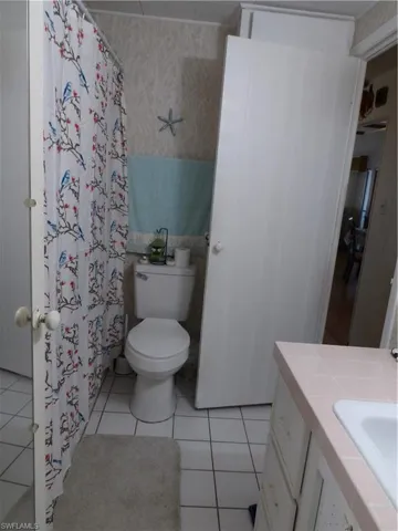 Full bath with vanity, a shower with shower curtain, wallpapered walls, and light tile patterned flooring