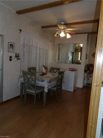 Dining room with wood finished floors, wallpapered walls, a ceiling fan, and beam ceiling