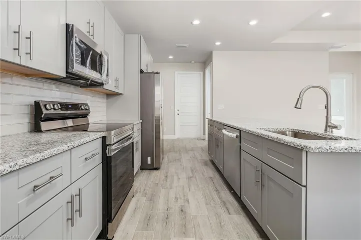 Kitchen with appliances with stainless steel finishes, light hardwood / wood-style flooring, sink, decorative backsplash, and light stone countertops Finishes may vary, pictures for illustration purposes only