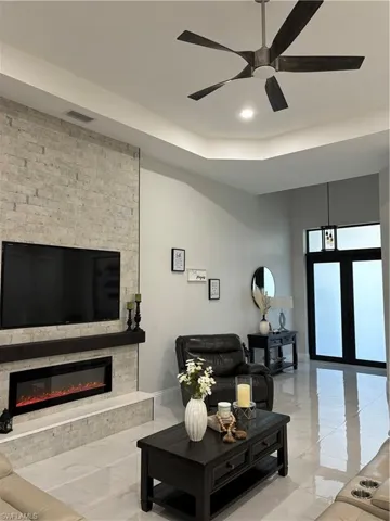 Living room with tile flooring, ceiling fan, a tray ceiling, and a fireplace
