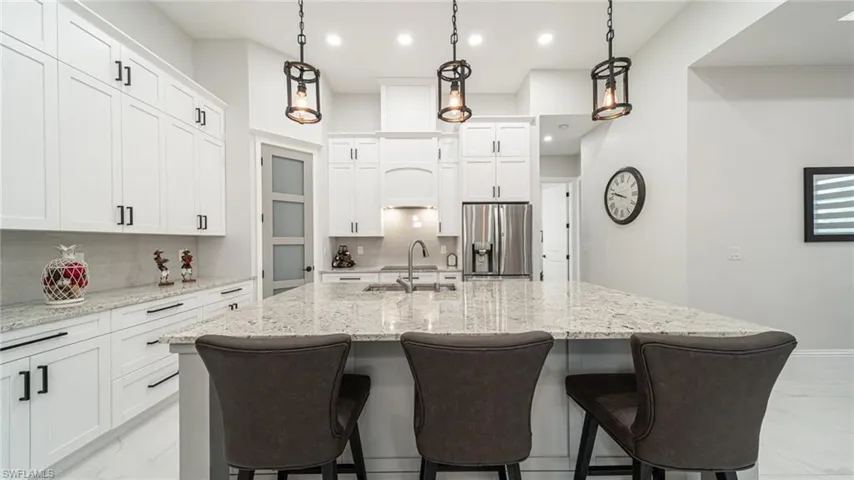 Kitchen featuring backsplash, hanging light fixtures, stainless steel fridge, and a kitchen island with sink