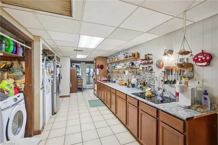 Bar featuring open shelves, washer / clothes dryer, a paneled ceiling, brown cabinets, and light tile patterned floors