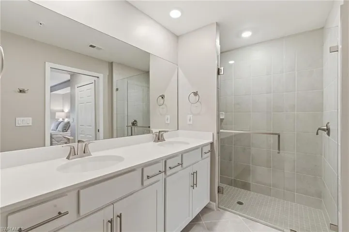 Ensuite bathroom with double vanity, a shower stall, recessed lighting, and light tile patterned flooring