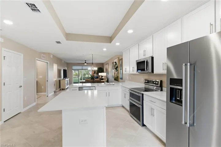 Kitchen featuring stainless steel appliances, open floor plan, decorative light fixtures, white cabinets, and a tray ceiling