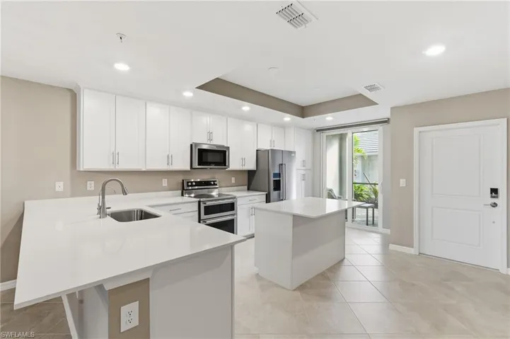 Kitchen with white cabinets, stainless steel appliances, a kitchen bar, a center island, and a peninsula
