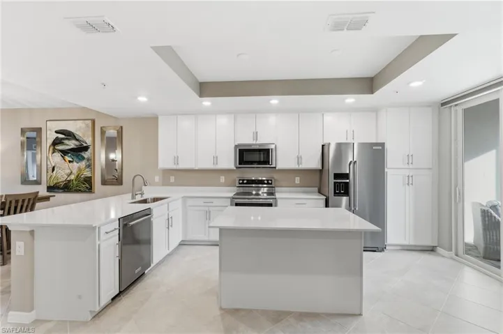 Kitchen with appliances with stainless steel finishes, a tray ceiling, white cabinetry, a center island, and recessed lighting