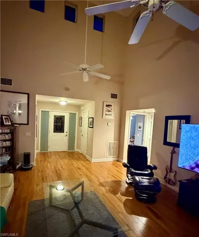 Living area with light wood-type flooring, a ceiling fan, and a high ceiling
