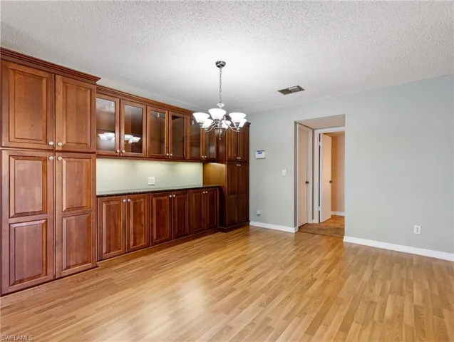 Kitchen with a notable chandelier, decorative light fixtures, light hardwood / wood-style flooring, and a textured ceiling