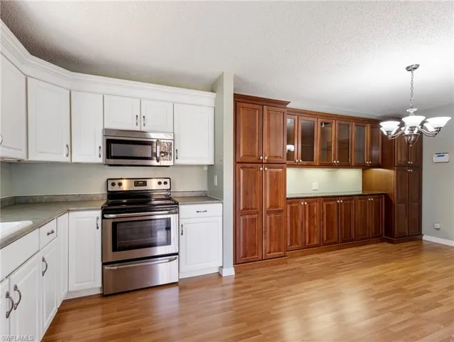 Kitchen featuring white cabinetry, decorative light fixtures, a chandelier, light wood-type flooring, and appliances with stainless steel finishes