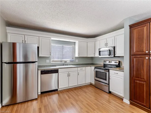 Kitchen featuring appliances with stainless steel finishes, sink, white cabinets, and light wood-type flooring