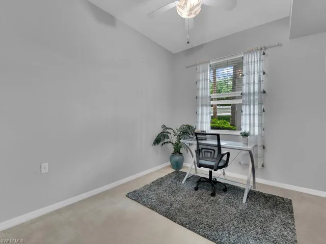 Carpeted office space featuring ceiling fan and baseboards
