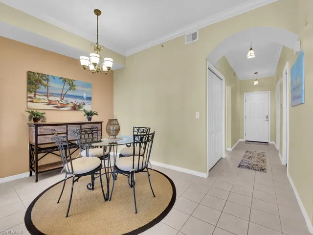 Dining space with light tile patterned floors, arched walkways, ornamental molding, and a chandelier