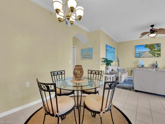 Dining area featuring arched walkways, a chandelier, light tile patterned floors, crown molding, and ceiling fan