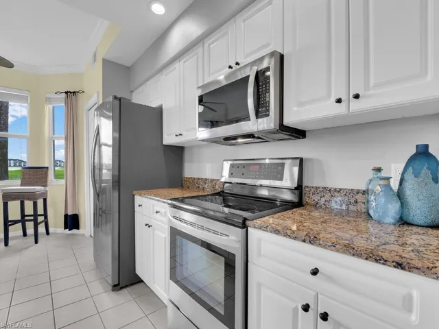 Kitchen featuring appliances with stainless steel finishes, white cabinetry, crown molding, light tile patterned floors, and stone counters