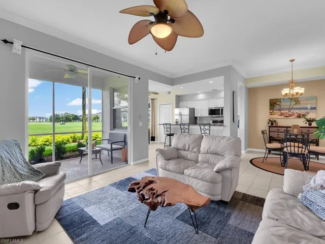 Living room featuring light tile patterned floors, ceiling fan, a chandelier, ornamental molding, and view of golf course