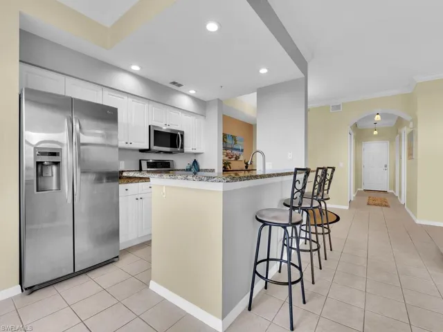 Kitchen featuring stainless steel appliances, arched walkways, dark stone counters, light tile patterned floors, and a kitchen bar
