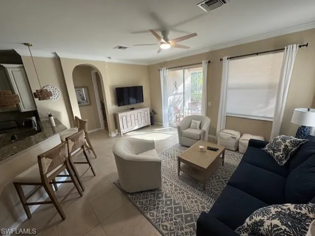 Tiled living area with arched walkways, ornamental molding, and ceiling fan