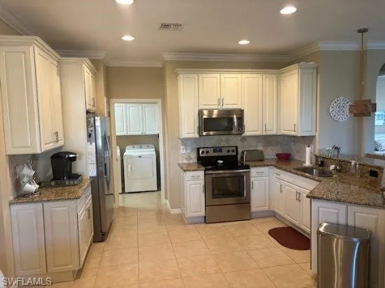 Kitchen featuring dark stone countertops, stainless steel appliances, backsplash, washer / clothes dryer, and ornamental molding