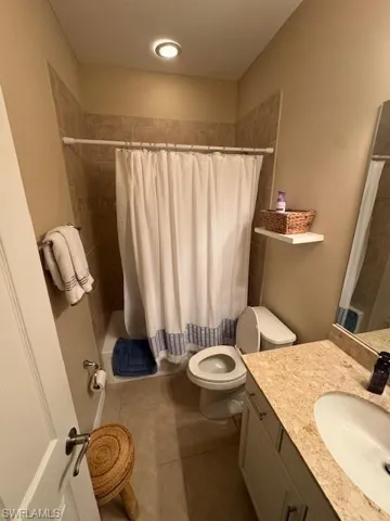 Bathroom featuring vanity, shower / bath combo with shower curtain, and dark tile patterned flooring