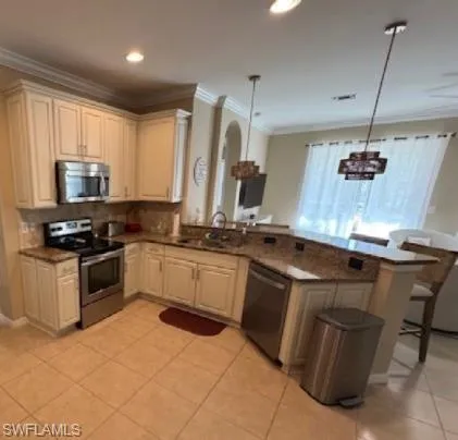 Kitchen with a peninsula, appliances with stainless steel finishes, hanging light fixtures, dark stone countertops, and tasteful backsplash