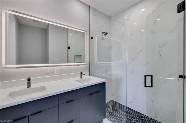 Master bathroom with marble finish shower, frameless shower door, double vanity, and LED-lighted mirror