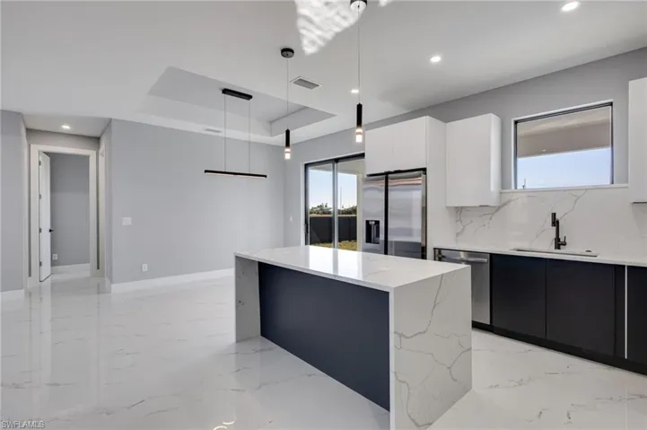 Dual-tone kitchen with modern cabinets, large island, stainless steel appliances, and hanging light fixtures