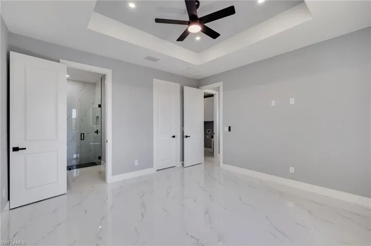 Master bedroom with connected bathroom, recessed lighting, tray ceiling, a ceiling fan, and light marble finish floors