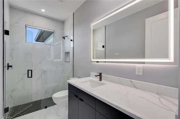 Full second bath featuring a large elegant vanity, a marble finish shower, frameless shower doors, and LED lighted mirror