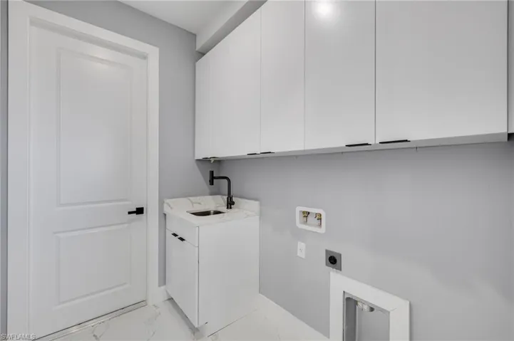 Laundry room with light marble finish flooring, upper cabinets, deep laundry sink, and washer/dryer hookups
