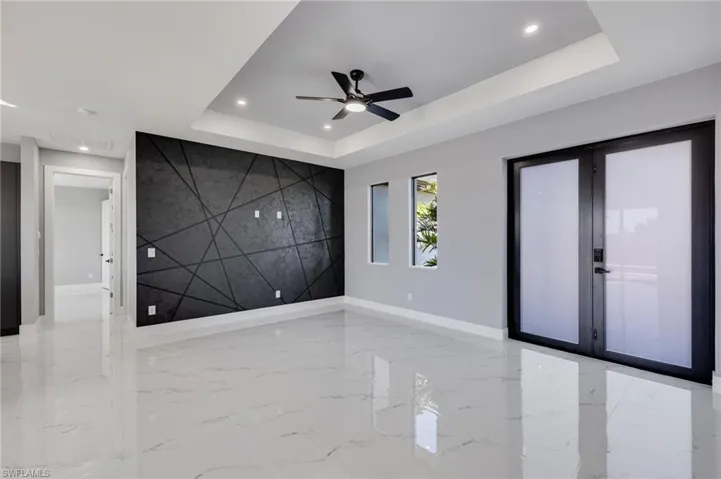 Living room with an accent wall, elegant doors, recessed lighting, ceiling fan, a tray ceiling, and light marble finish floors